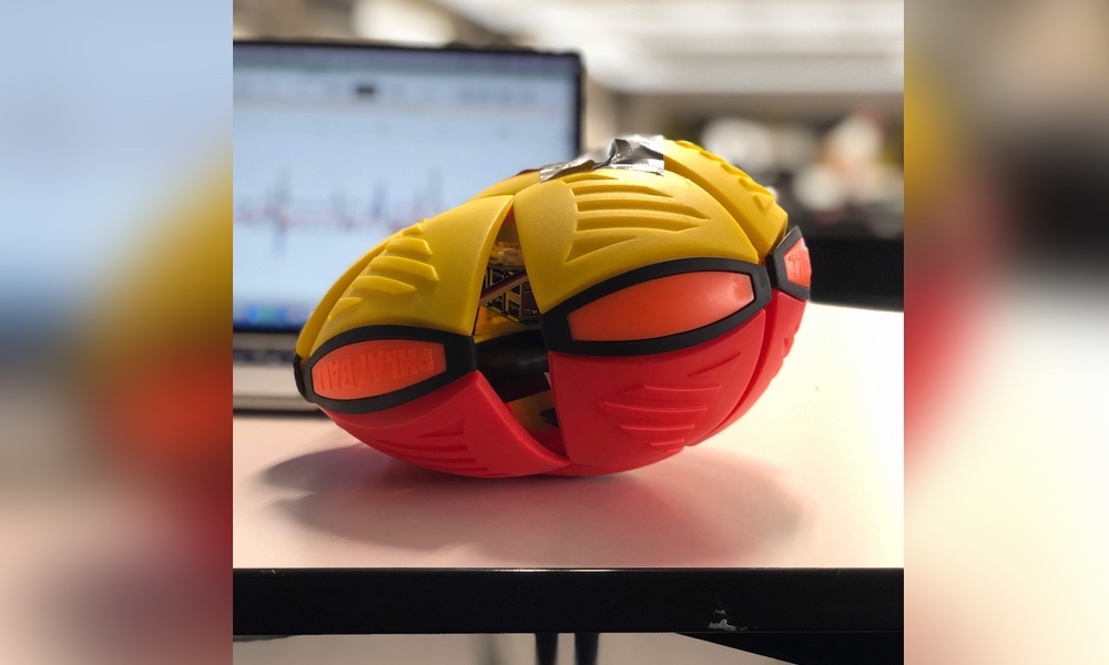 A ball with a Raspberry Pi inside. In the background is a laptop displaying graphs.